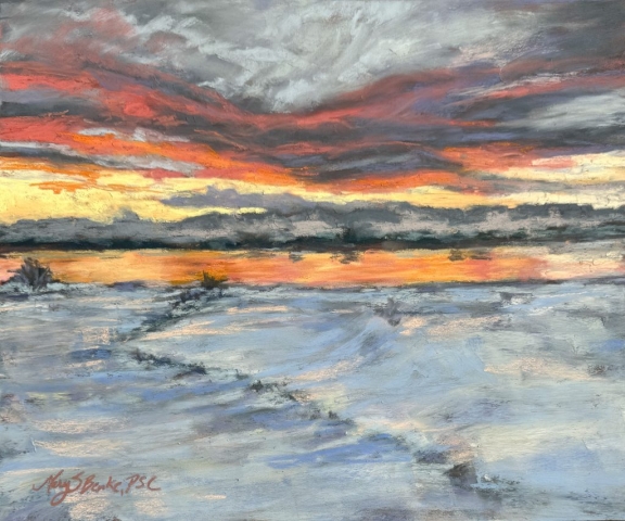 A vibrant winter sunset sky, filled with hues of orange, gold, and gray, stretches above a serene body of water reflecting the dramatic colors. A snowy foreground in blues, lavenders, and whites contrasts with the fiery sky. The pastel marks give a sense of movement to the clouds and water, capturing the dynamic beauty of the scene by Mary Benke
